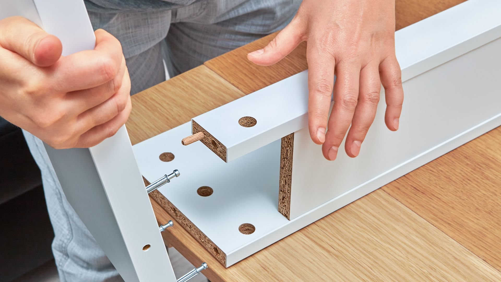 Hands assembling white furniture with wooden dowels and metal screws